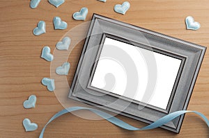 It`s a boy announcement concept: blank photo frame on a wooden table sorrounded by light blue hearts and a ribbon