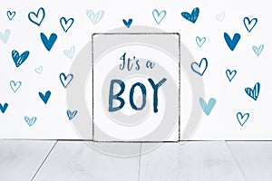 It`s a boy new born baby text on sign board with cute little blue hearts on white background