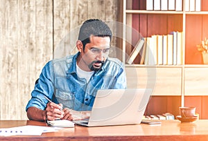 30s handsome businessman take a short note on paper while reading article from internet.  Modern arab businessman in casual