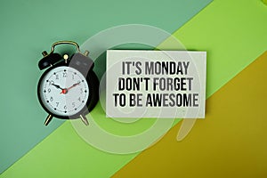 It\'s Monday Don\'t Forget To Be Awesome text on paper card with alarm clock on green and yellow geometric background photo