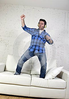 20s or 30s man jumped on couch listening to music on mobile phone with headphones playing air guitar photo