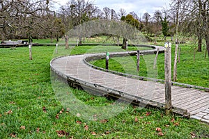 S-shaped winding wooden walkway bridge over green grass with hiking trail signs