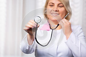 It`s time for a check up in clinic, female doctor holds stethoscope stretched to camera. Health care concept with side white spac