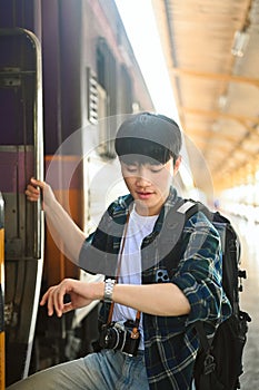 It's time to get on the train. Traveler male with backpack checking time on wrist watch and getting on the train