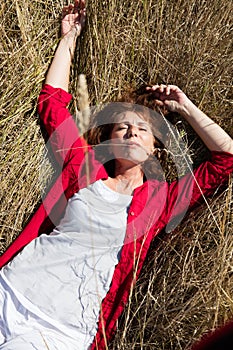 50s woman enjoying sun warmth alone sleeping on dry grass