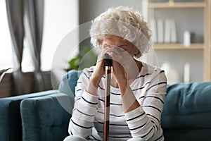 70s woman hides her face with hands holding walking stick