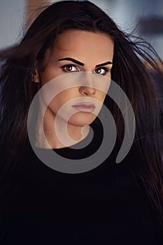 25s woman portrait with fluttering black hairs looking at camera posing indoors