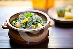 saag aloo in a ceramic pot on a wooden table