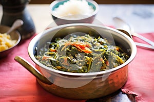 saag aloo in a copper serving bowl, rice behind