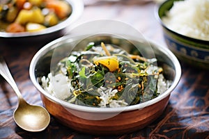 saag aloo in a copper serving bowl, rice behind