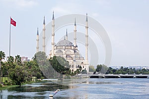 Sabanci Merkez Cami Central Mosque with Tash KÃ¶prÃ¼ Bridge on the Seyhan River with Turkish flags next to it in cloudy weather in