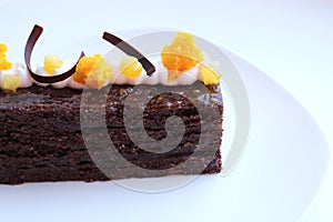 Sacher Torte cake with apricot pieces and orange microwave sponge decoration on white plate