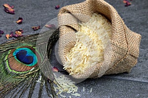 A sack of rice with a peacock feather on a stone grey background with copy space