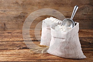 Sacks with flour and wheat spikes on wooden background. Space for text