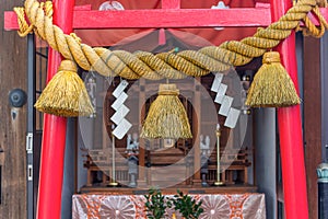 Sacred rope, or shimenawa, on red torii gate to small local shinto shrine, Kanazawa, Japan