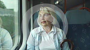 Sad 50s 60s senior woman looking out of a train window, thinking of something seating near the window in city train