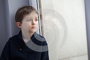 Sad 7 years boy child looking out the window.