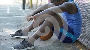 Sad African-American basketball player sitting on the ground, lack of motivation