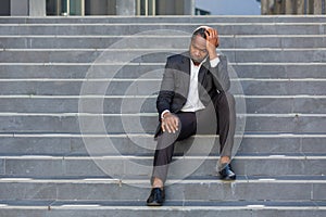 Sad african american businessman sitting on stairs outside office building, man in business suit bankrupt fired from job