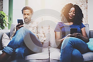 Sad african american couple relaxing together on the sofa.Young black man and his girlfriend using mobile devices while