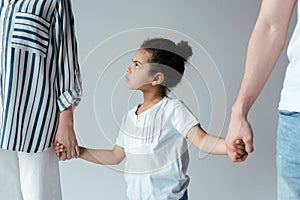 Sad african american kid holding hands with divorced foster parents