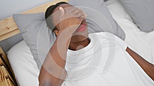 Sad african-american woman covering eyes with hand, lying on bedroom bed, sightless, hiding, rejection concept