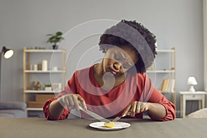 Sad african american woman frowning holding cutlery looking at apple piece