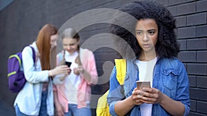 Sad african schoolgirl reading humiliating message, cyber bullying embarrassment