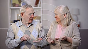 Sad aged couple holding coins looking each other, social insecurity, poverty