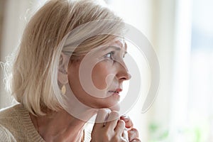Sad aged woman crying near window feeling lonely