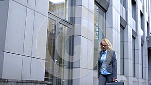 Sad aged woman getting work walking along office building, occupational burnout