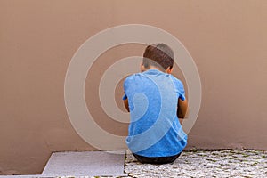 Sad alone boy sitting on the ground behind the wall outdoor