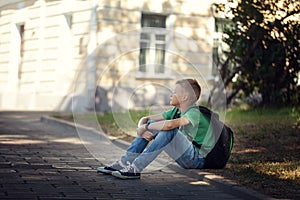 Sad alone boy sitting on road in the park outdoors