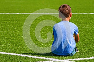 Sad alone boy sitting in soccer field stadium outdoors