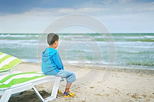 Sad alone kid sitting on beach, looking at sea and thinking. The end of summer. sadness about end of vacation