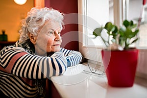 Sad alone senior woman looking through window