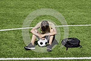 Sad alone teenage boy sitting in empty school sport stadium outdoors. Emotions, defeat, lost game, difficulties