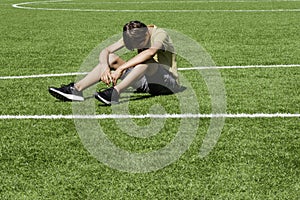 Sad alone teenage boy sitting in empty school sport stadium outdoors. Emotions, difficulties, depresion, problems of