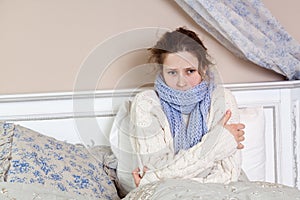 Sad alone young woman in white sweater and blue scarf feeling cold sick and resting home in bed