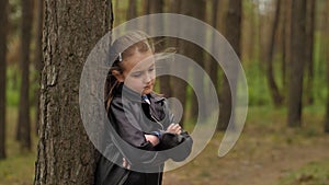 A sad angry little girl standing in front of a tree in the forest