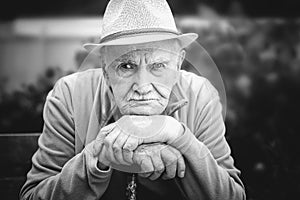 Sad, angry old man in a hat is sitting in an open-air garden. the concept of loneliness and lonely old age. Black and white