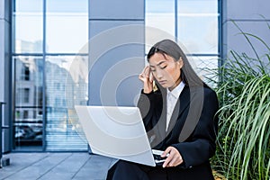 Sad and anxious Asian student, received disappointing news about entering university and college, sitting on a bench with a laptop