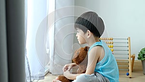 Sad Asian boy sits with his head down and looks out the door at his favorite doll