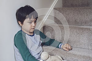 Sad asian boy wearing pyjamas sitting at carpet staircase in the morning, Lonely kid looking dow with sad face, Depressed child