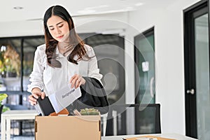 Sad Asian female office worker packing her stuff into a cardboard box in the office, quitting her job