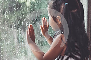 Sad asian little girl looking outside through the window photo