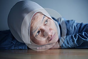 Sad Asian muslim woman laying her head down on table and looking up with blank stare thinking about something