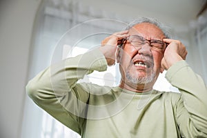 Sad Asian senior man chronic migraine pain massaging