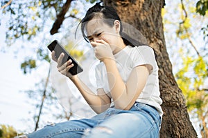 Sad asian student victim of cyber bullying online sitting alone outdoor at school,teenage girl receiving text message at mobile