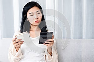 Sad Asian woman holding calculator with list of debt, expenses on notepad , female having financial problem during quarantine